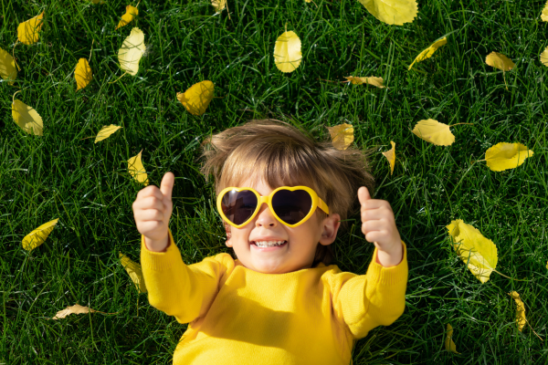 jongetje liggend in het gras met een zonnebril op en steekt zijn duimen omhoog