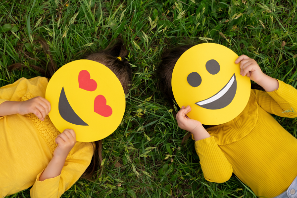 twee kinderen liggend in het gras met een masker van een blije emoji voor hun gezicht